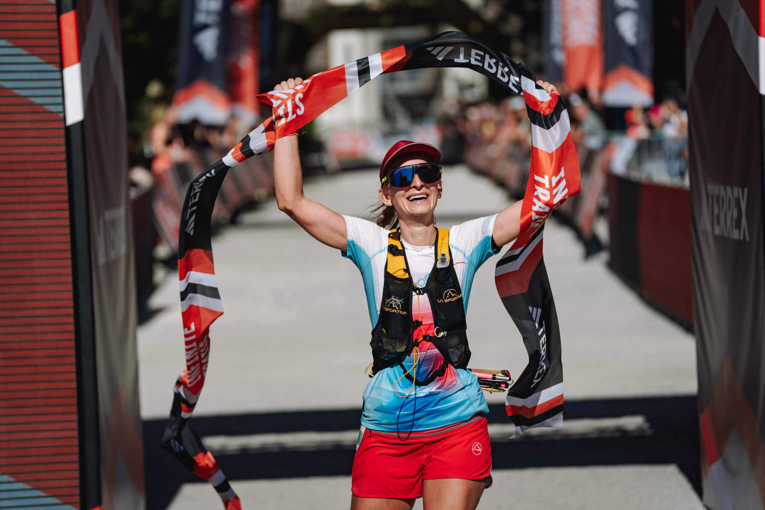 Läuferin jubelt beim Zieleinlauf mit einer Flagge, umgeben von Zuschauern und Festlichkeiten.