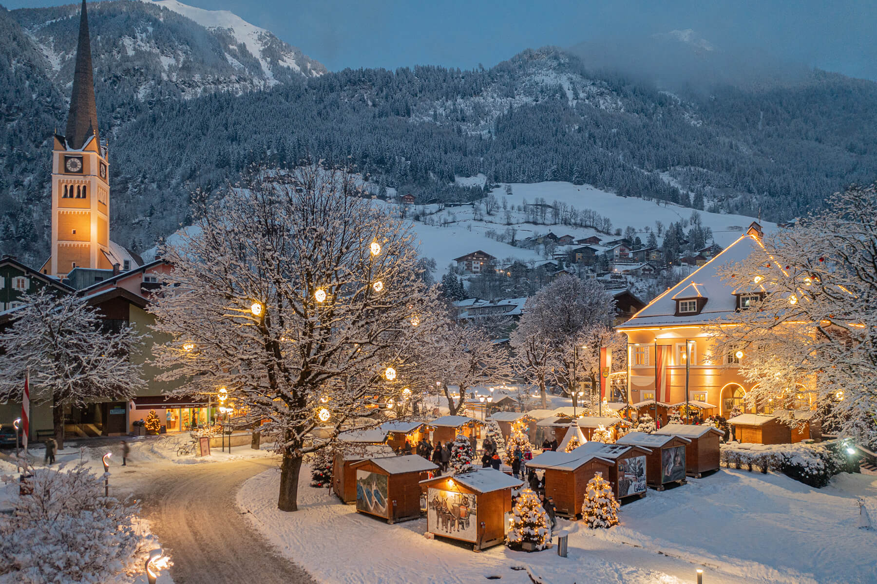 Winterliche Landschaft von Bad Hofgastein mit verschneiten Hütten und beleuchtetem Kirchturm.