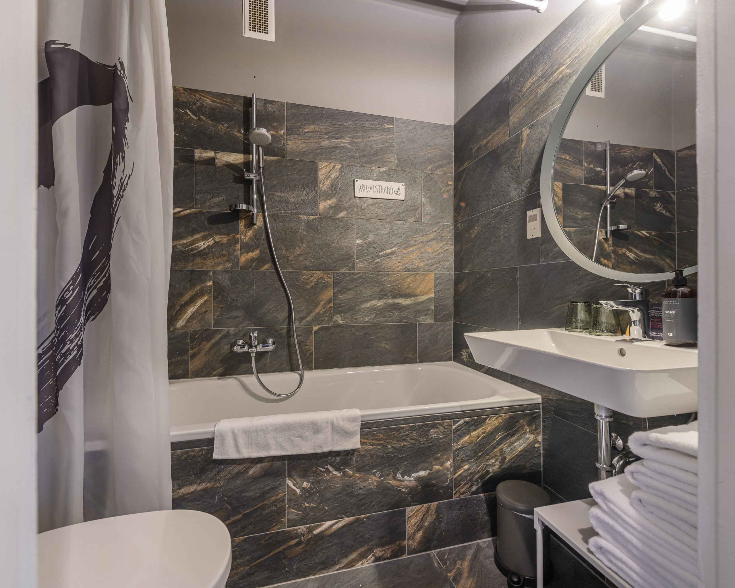 Modernes Bad mit Badewanne, Duscharmatur, Waschbecken und dunklen Marmorfliesen