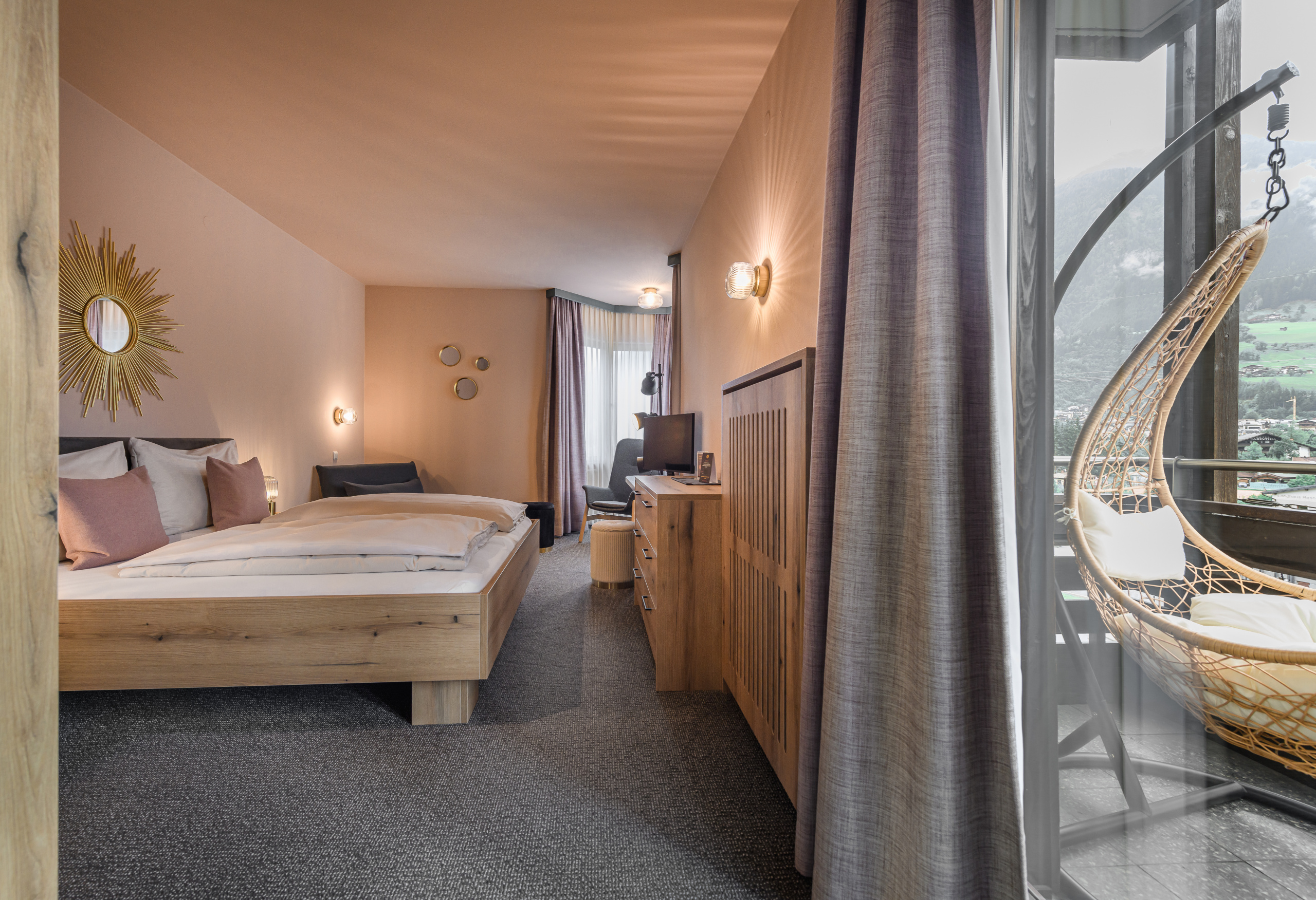 Doppelzimmer mit Holzbett, Sitzbereich, Fernseher und Hängesessel auf dem Balkon mit Bergblick