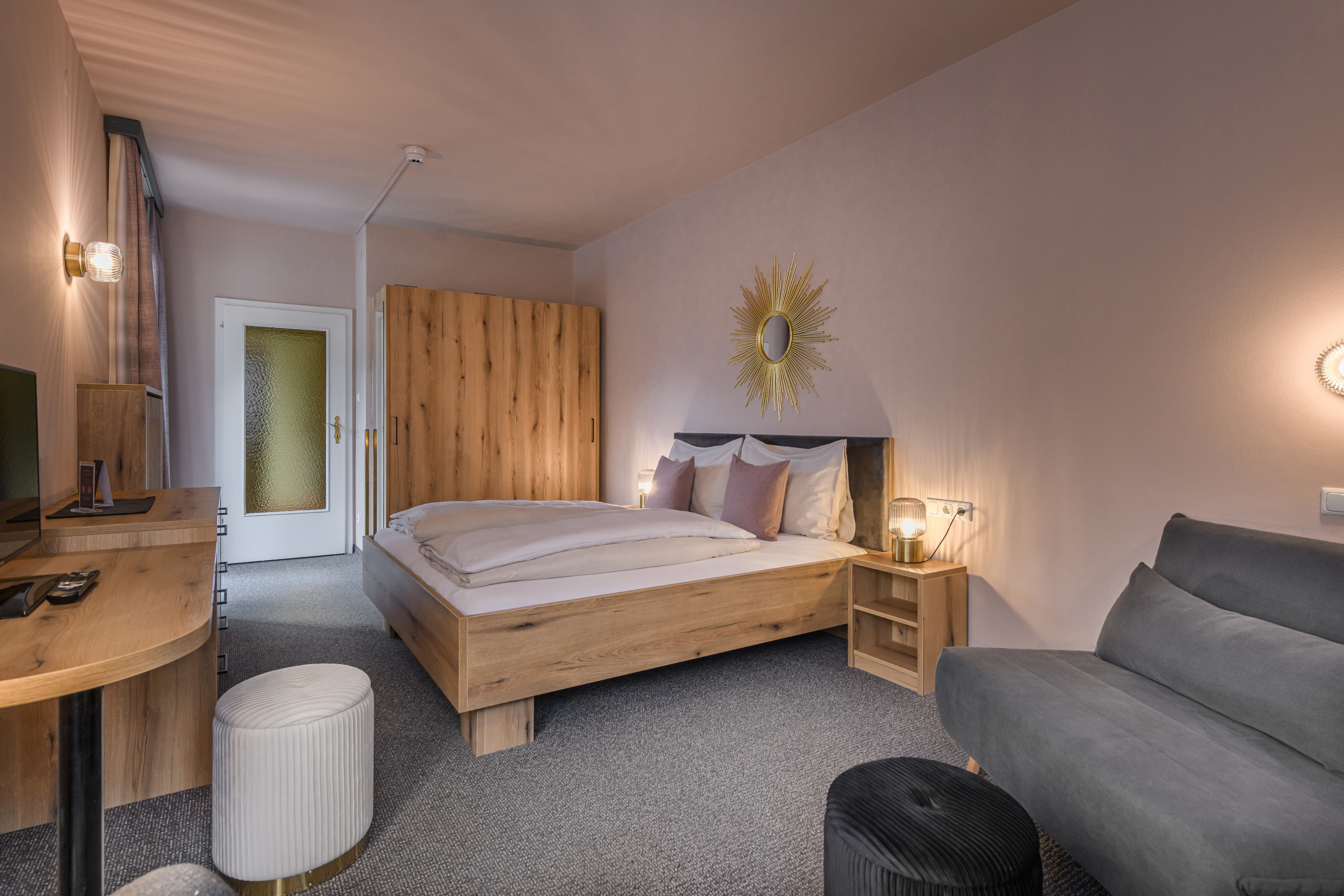 Doppelzimmer mit Holzbett, grauem Sofa, Schreibtisch und Kleiderschrank