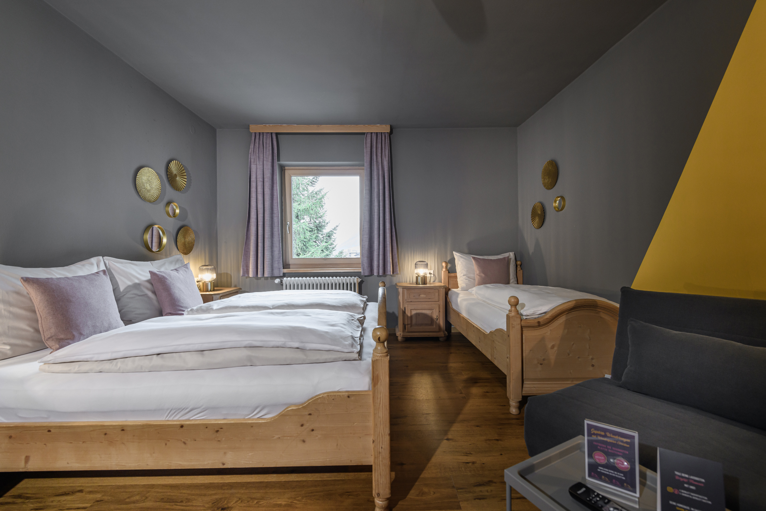Vierbettzimmer mit Doppelbett, Einzelbett, Schlafsofa und Fenster mit lila Vorhängen