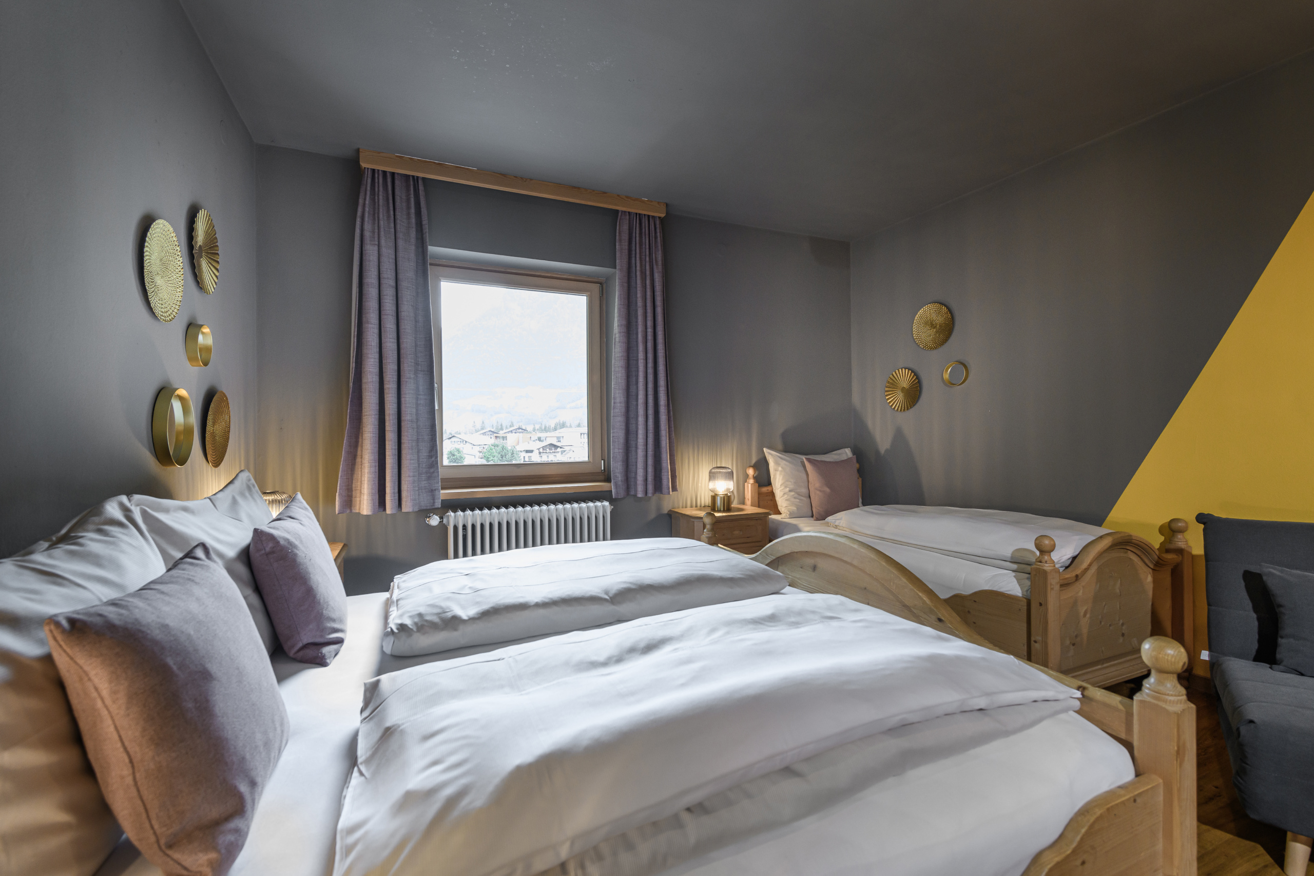Vierbettzimmer mit Doppelbett, Einzelbett, grauen Wänden und Fenster mit Blick nach draußen