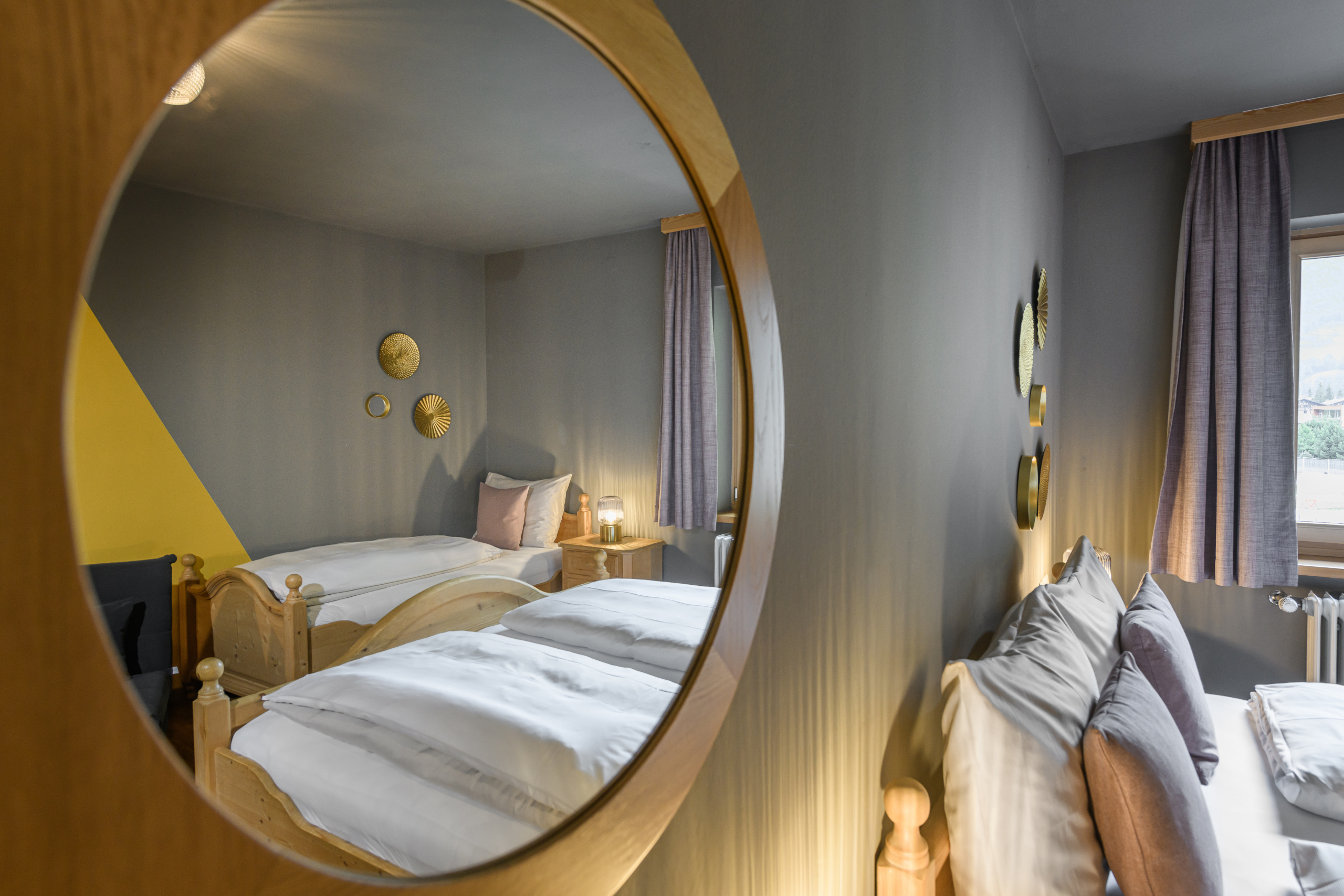 Vierbettzimmer mit zwei Holzbetten, grauen Wänden, runden Spiegeln und Vorhängen