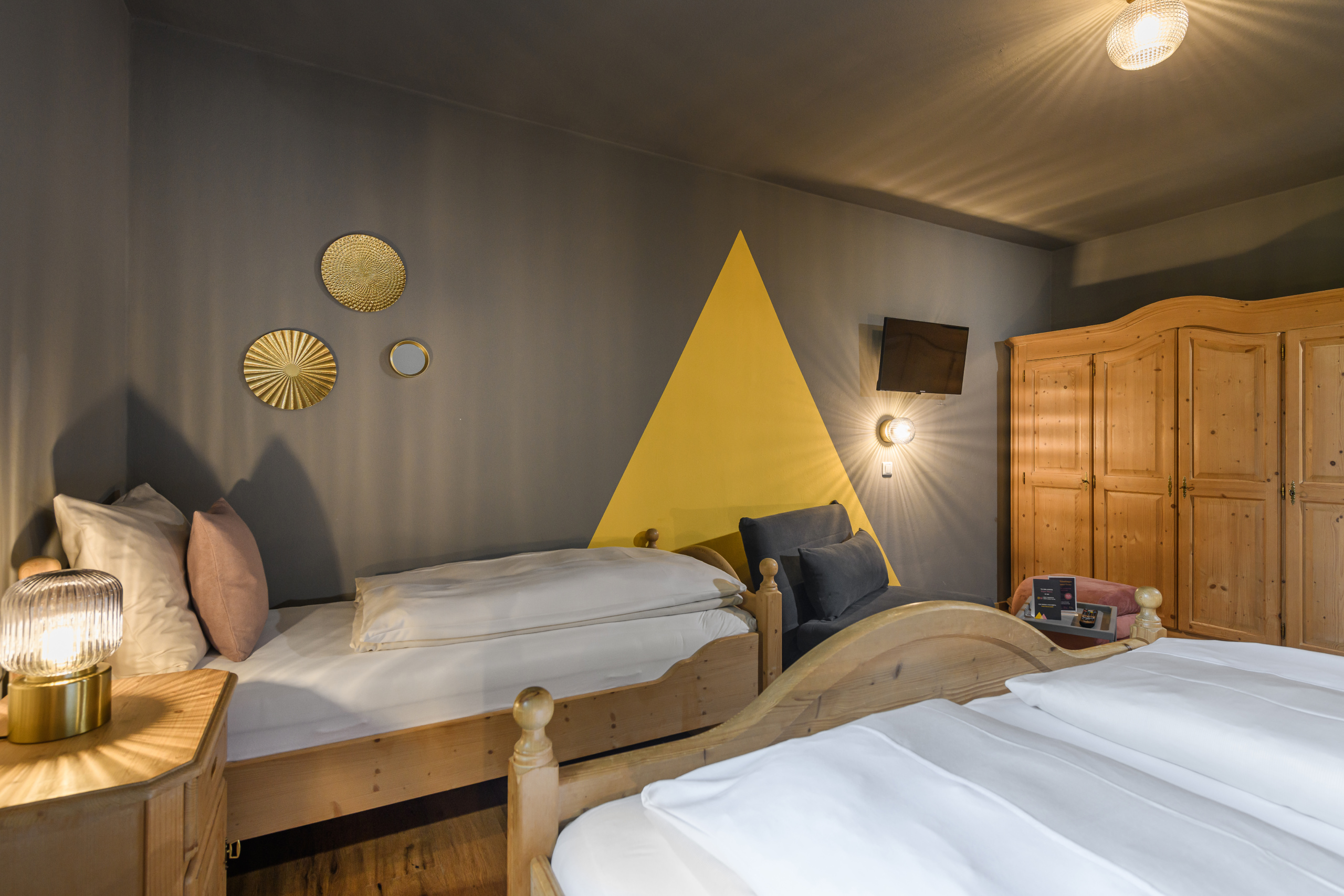 Vierbettzimmer mit zwei Holzbettgestellen, gelber Wandgestaltung, Sesseln und großem Holzschrank