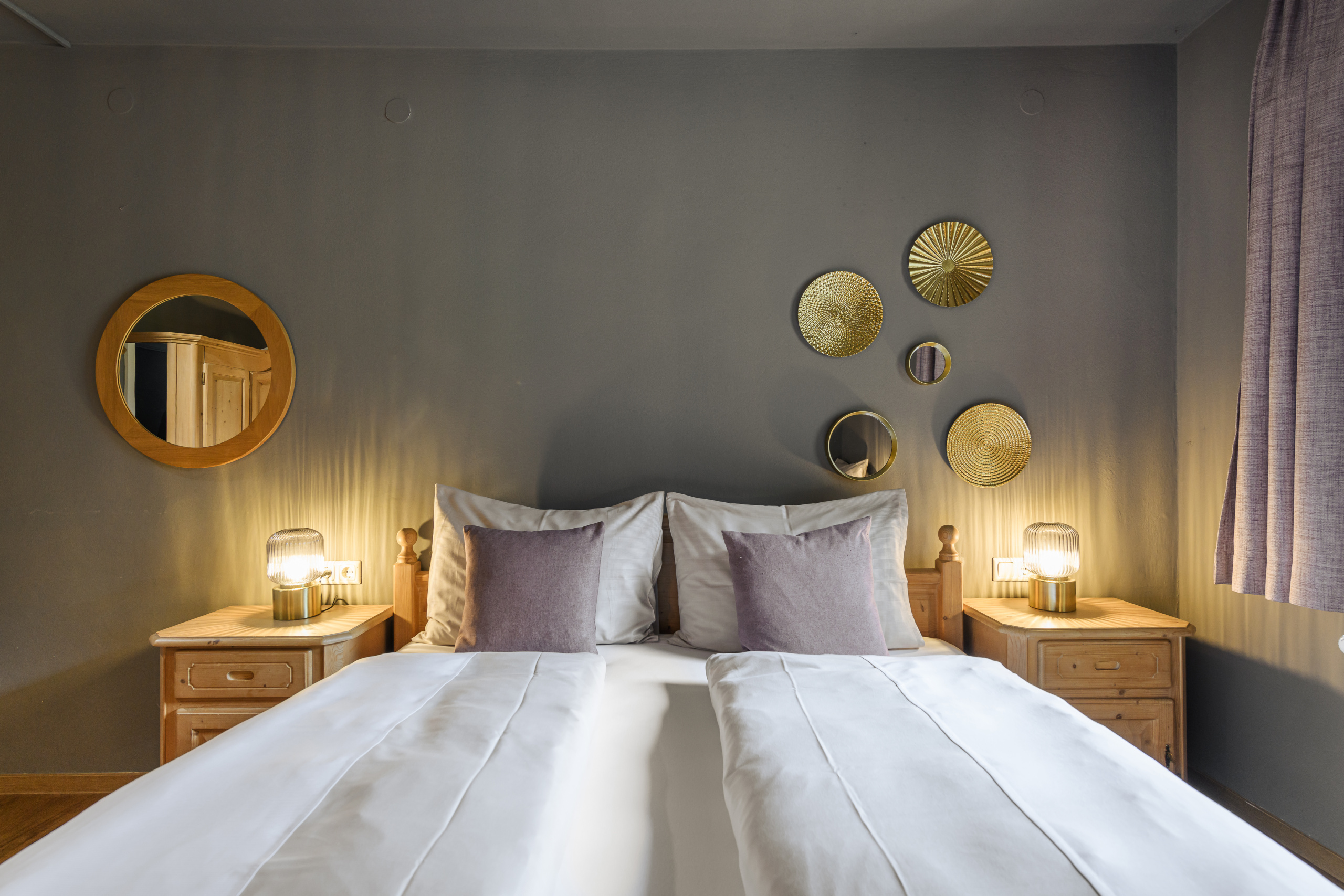 Doppelbett mit weißen Decken, Nachttischen und goldfarbenen Wandspiegeln in einem Hotelzimmer