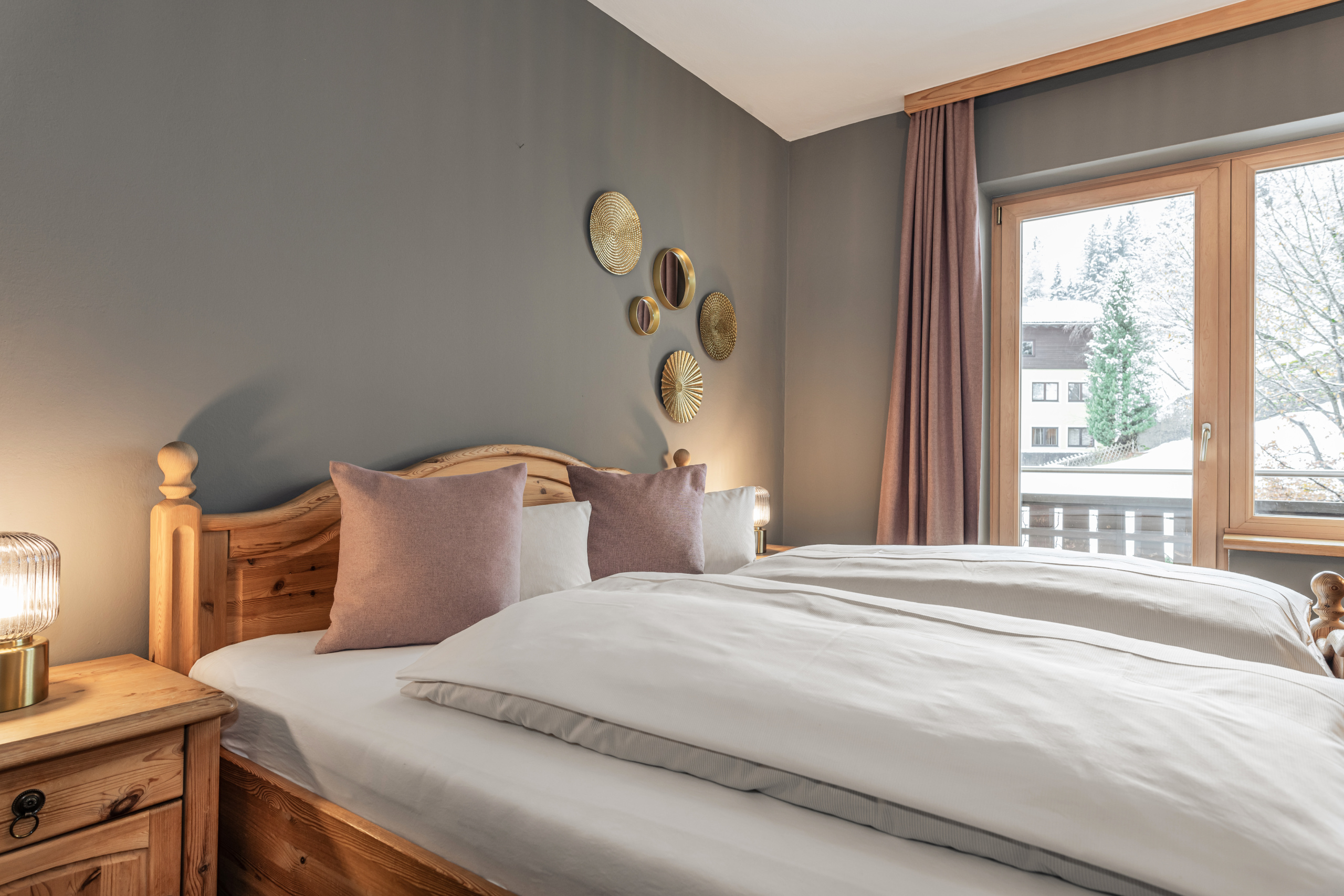 Doppelbett mit Holzkopfteil in einem Zimmer mit grauer Akzentwand und Balkonfenster