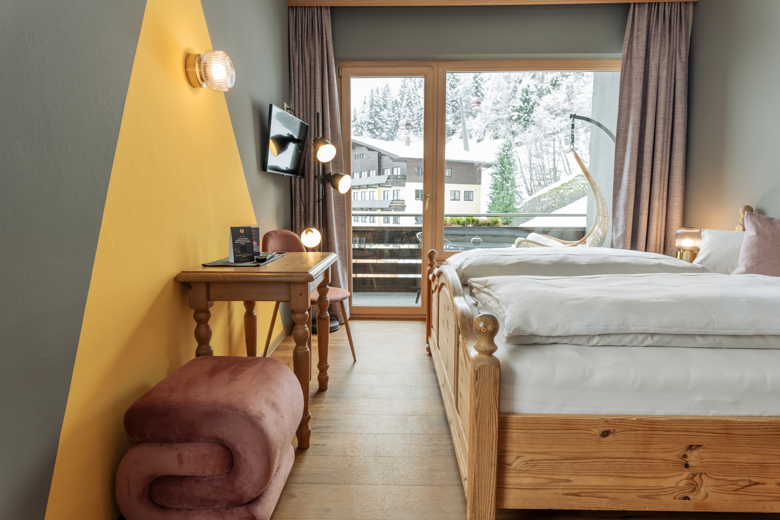 Doppelzimmer mit Holzbett, Schreibtisch und Balkon vor verschneiten Bäumen