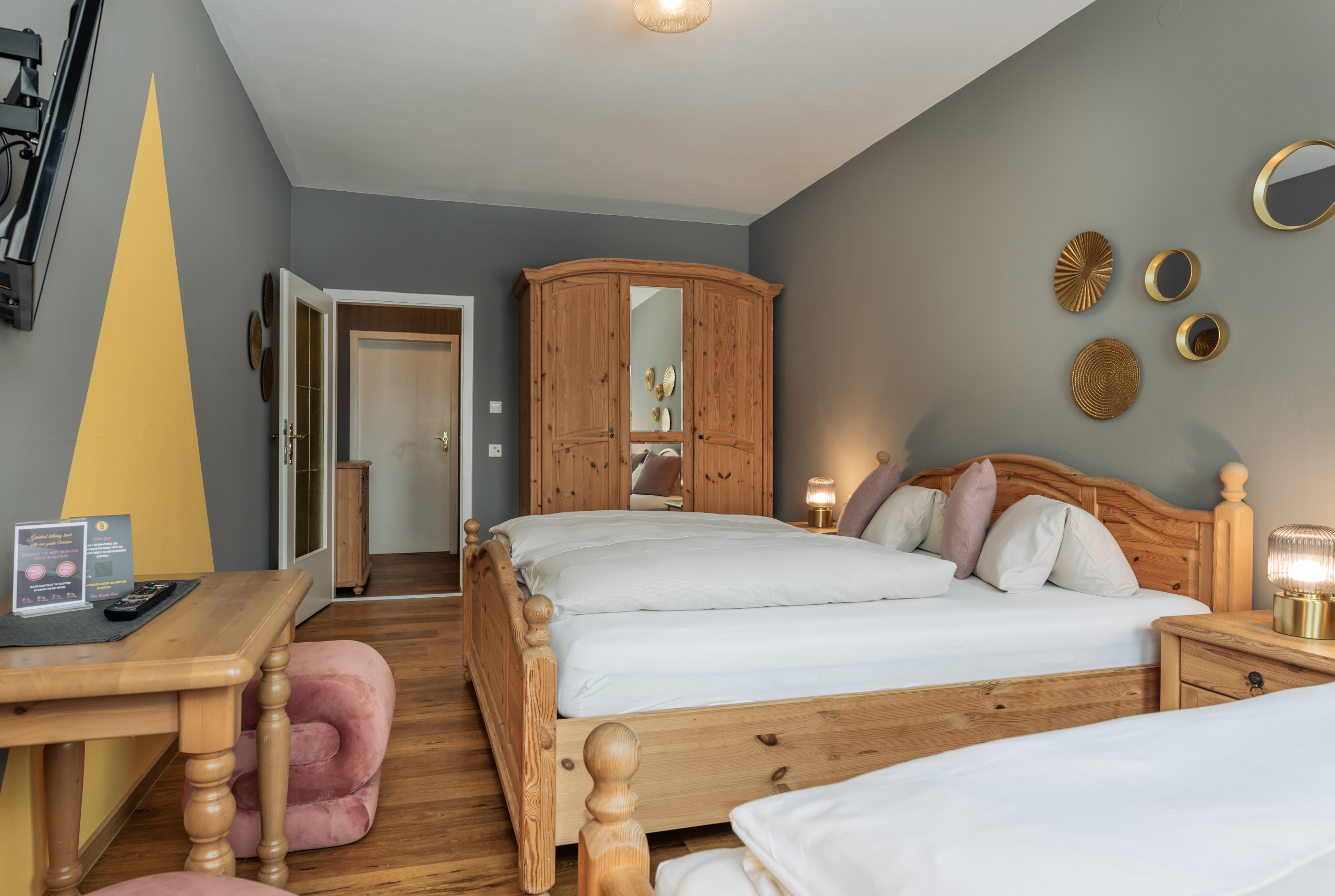 Dreibettzimmer mit Doppelbett, Einzelbett, Holzmöbeln, Schreibtisch und grauen Wänden