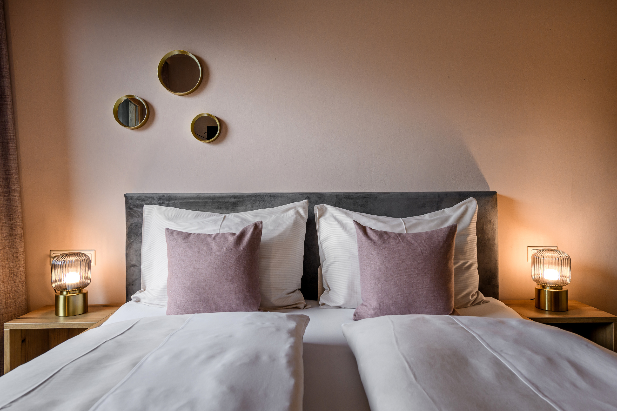 Gemachtes Doppelbett mit weißen Decken, roséfarbenen Kissen und zwei Nachttischlampen in warm beleuchtetem Zimmer