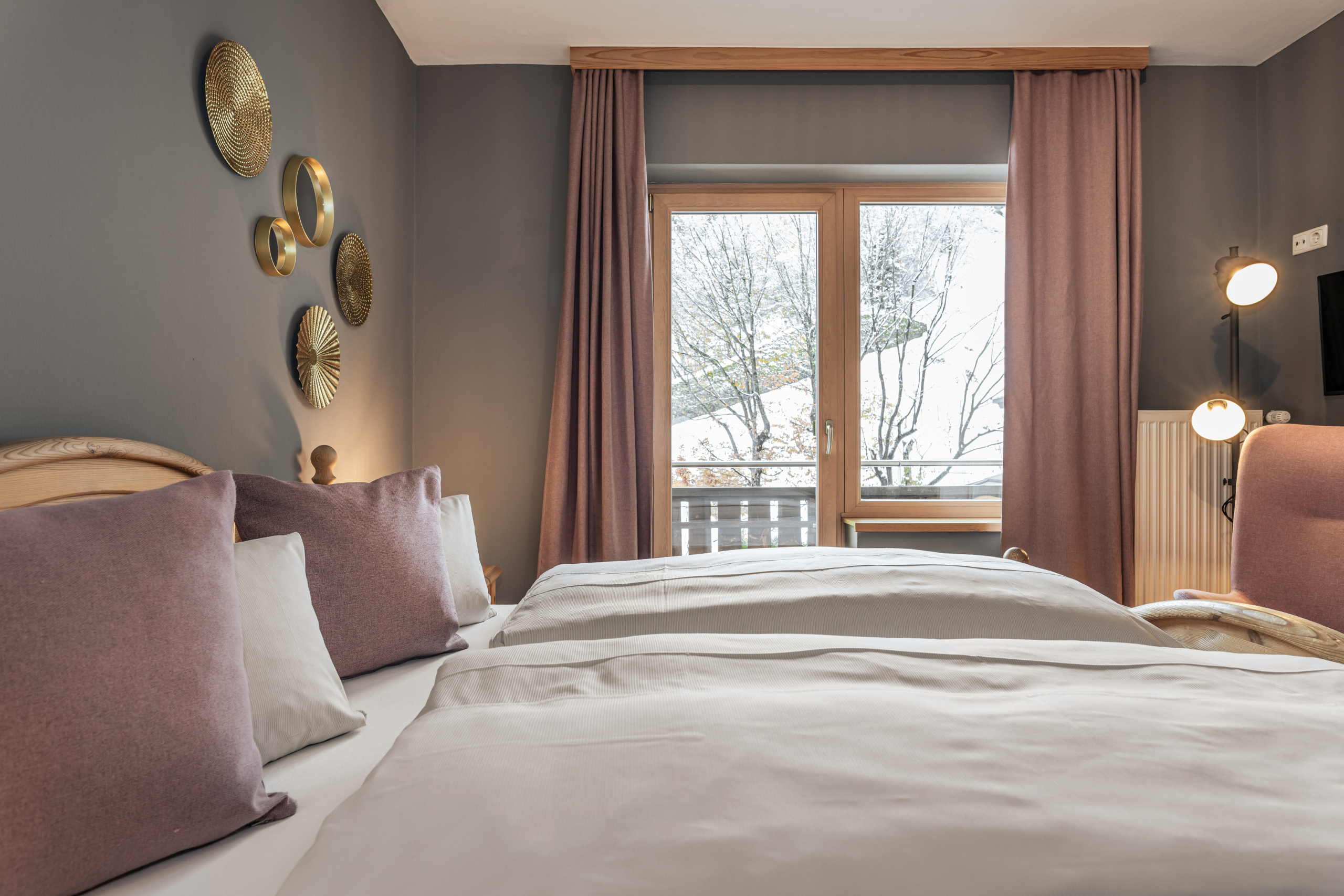 Doppelbett mit rosa Kissen in einem Zimmer mit Balkonfenster, Sessel und goldener Wanddekoration