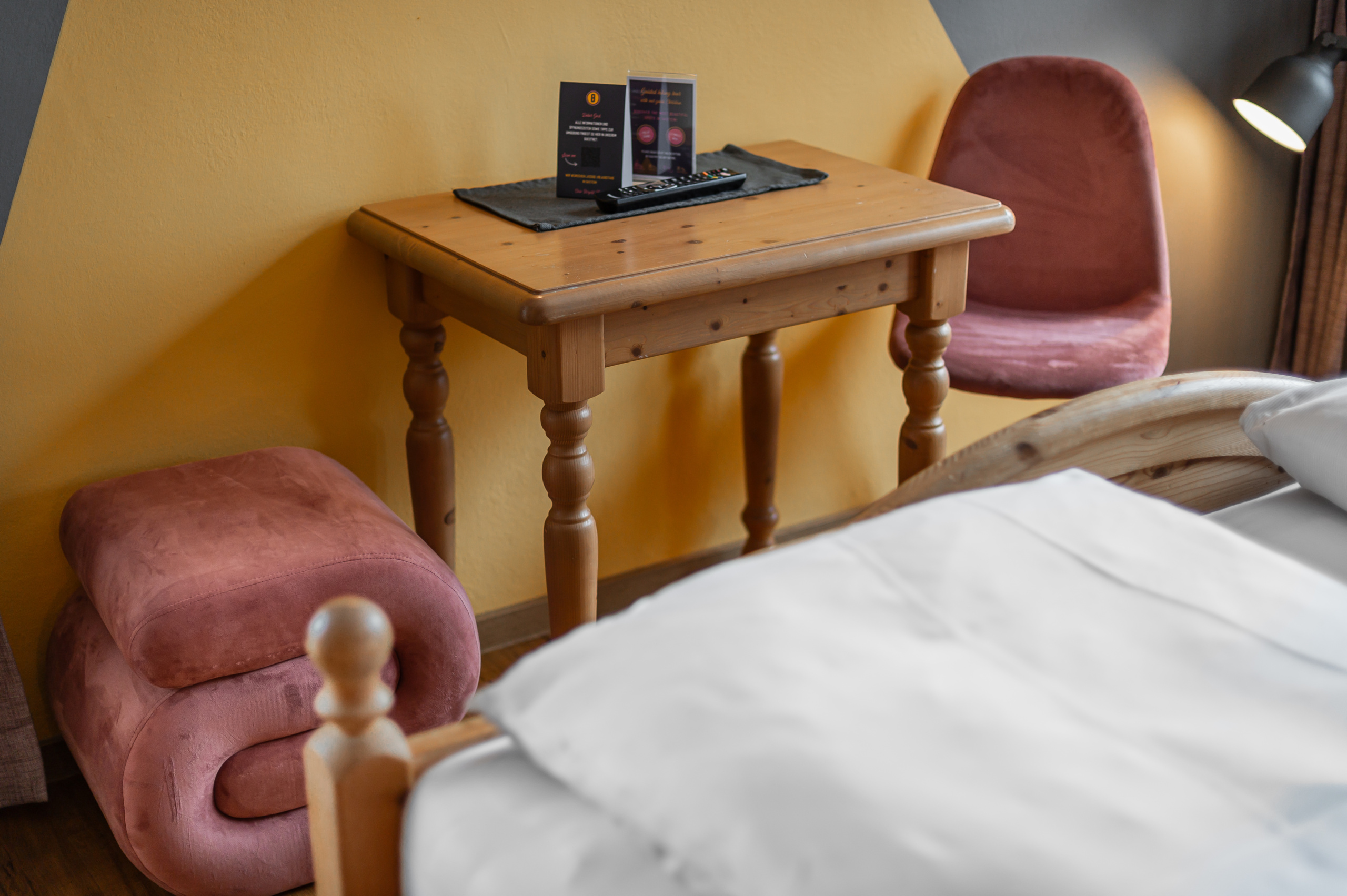 Doppelzimmer mit Holztisch, rosa Polstersessel und Bett mit weißer Bettwäsche