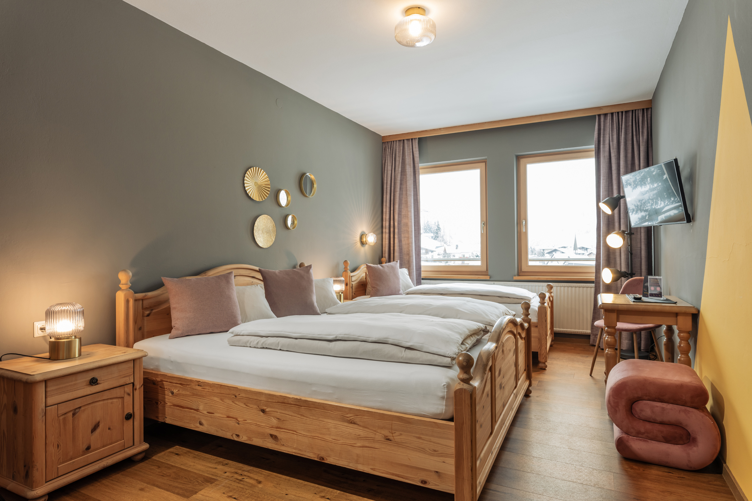 Dreibettzimmer mit zwei Holzdoppelbetten, Sitzhocker, Schreibtisch und zwei Fenstern
