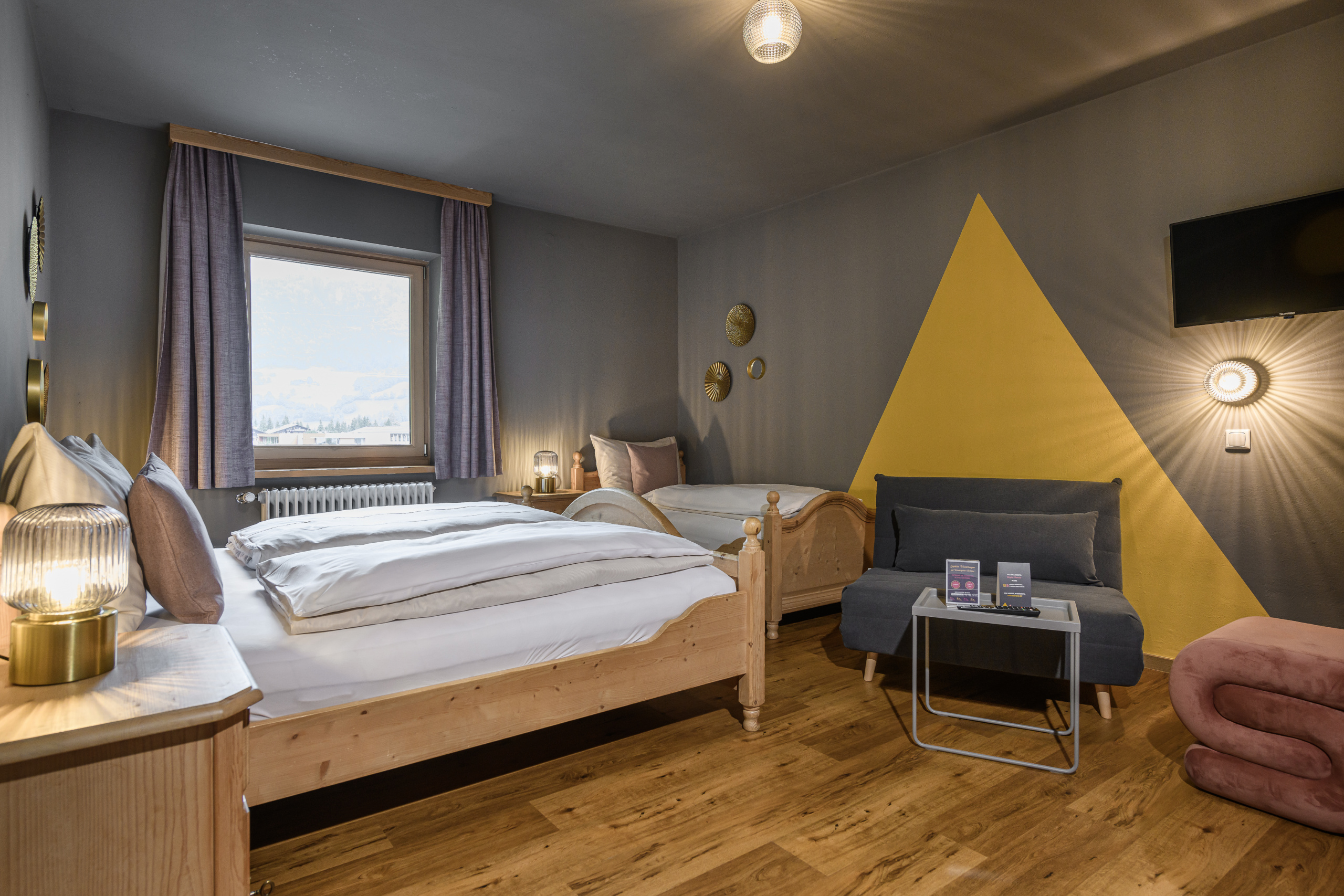 Vierbettzimmer mit Doppelbett, Einzelbett, Schlafcouch und Sitzbereich in Grau und Gelb