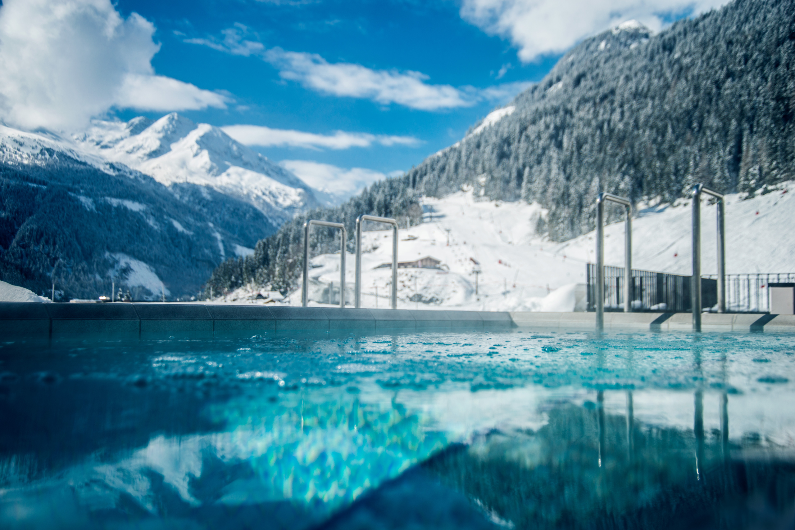 Außenbecken der Felsentherme Bad Gastein vor verschneiten Bergen und bewaldeten Hängen