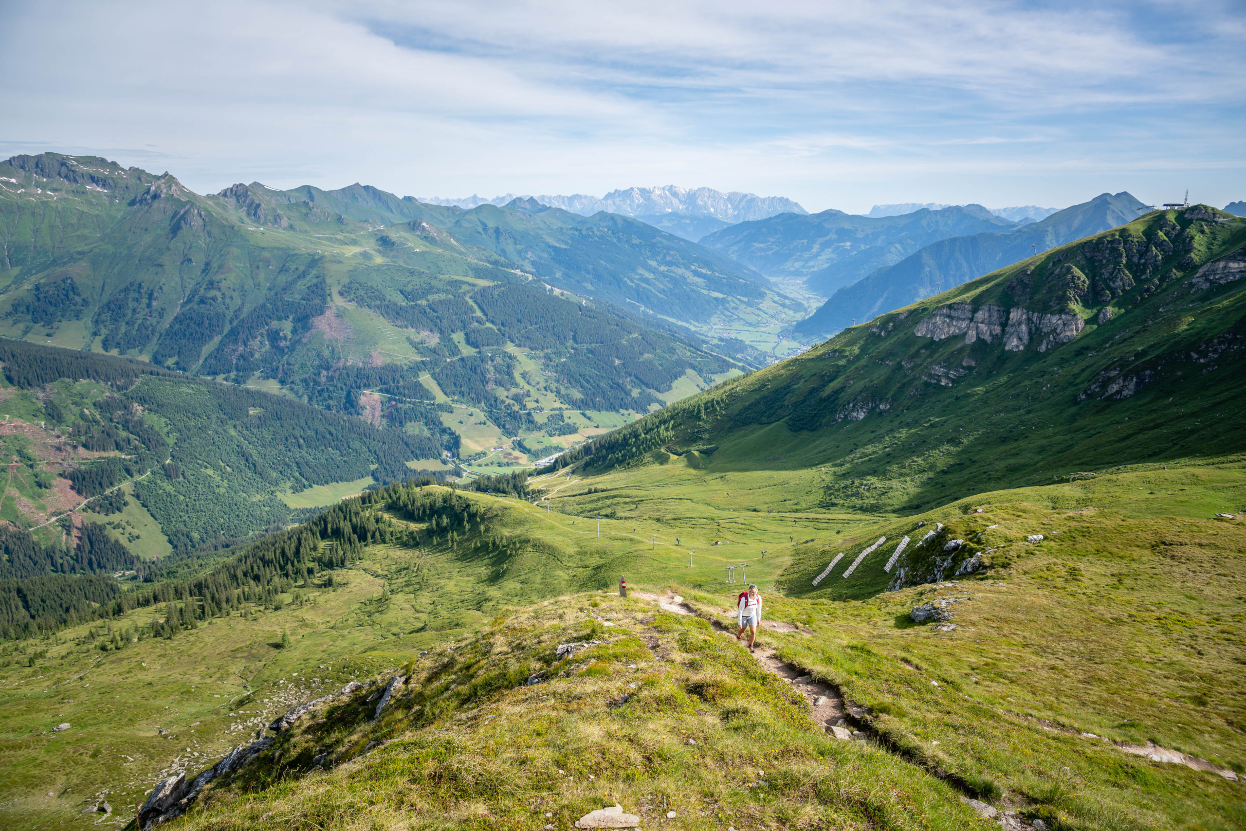 Wanderer auf schmalem Bergpfad mit Blick über grüne Almen und das weite Tal